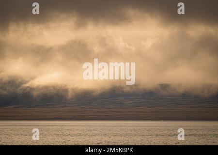 Die bergige Küste von Bylot Island in Nunavut, Kanada, ist teilweise von Wolken verdeckt. Stockfoto