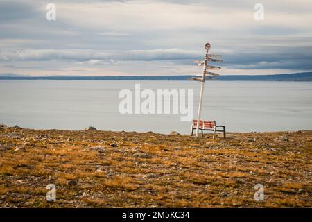 Parkbank und Entfernungsschild an einem Aussichtspunkt in Pond Inlet mit Blick auf den Eclipse Sound auf Baffin Island, Nunavut, Kanada. Stockfoto