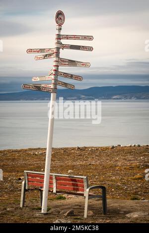 Parkbank und Entfernungsschild an einem Aussichtspunkt in Pond Inlet mit Blick auf den Eclipse Sound auf Baffin Island, Nunavut, Kanada. Stockfoto