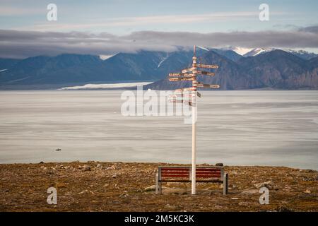 Parkbank und Entfernungsschild an einem Aussichtspunkt in Pond Inlet mit Blick auf den Eclipse Sound auf Baffin Island, Nunavut, Kanada. Stockfoto