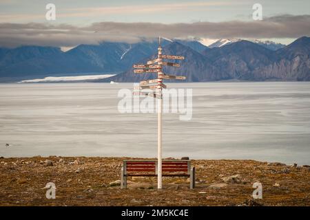 Parkbank und Entfernungsschild an einem Aussichtspunkt in Pond Inlet mit Blick auf den Eclipse Sound auf Baffin Island, Nunavut, Kanada. Stockfoto