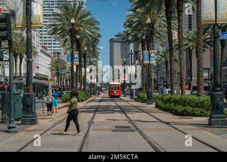 New Orleans, LA, USA – 14. Mai 2021: Von Palmen gesäumte Straße in der Innenstadt von New Orleans mit rotem Trolley auf Gleisen und vorbeilaufenden Menschen. Stockfoto