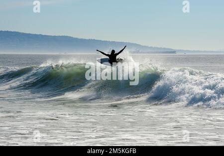 Surfer auf einer Welle am Venice Beach mit der Palos Verdes Halbinsel im Hintergrund in Südkalifornien. Stockfoto