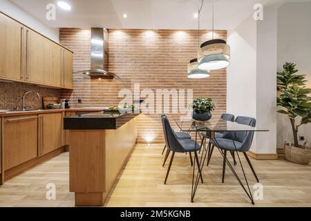 Apartment mit offener Küche mit Holzmöbeln, schwarzer Marmorarbeitsfläche und Schreibtisch aus Glas und Metall mit gepolsterten Stühlen aus blauem Samt Stockfoto