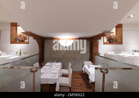 Reservierter Speisesaal eines Restaurants mit halbdurchsichtigen Glaswänden, Esstischen mit Tischdecken und weißen Polsterstühlen Stockfoto