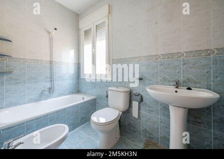 Badezimmer mit weißen Porzellan-Toiletten mit blauen Fliesen auf dem Boden und einer Halbwand mit Rand und hellen Fliesen darüber Stockfoto