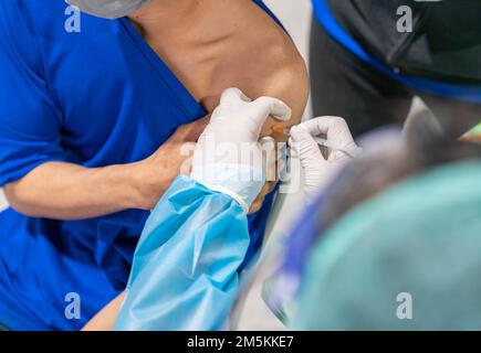 Arzt, der die Spritze hält, um die covid 19-Impfdosis in der Schulter des männlichen Patienten zu verabreichen. Grippe-Grippe-Impfstoffkonzept. Stockfoto