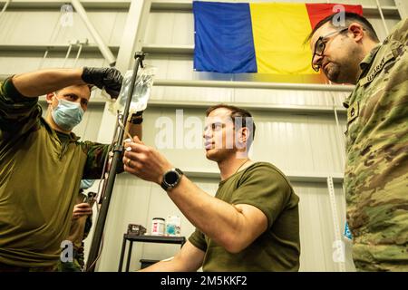 LUFTSTÜTZPUNKT MIHAIL KOGALNICEANU, RUMÄNIEN – USA Army Sgt. 1. Klasse Gorcyca von 1. Air Cavalry Brigade beobachtet belgische medizinische Soldaten während des Bluttransfusionstrainings am MK Air Base, Rumänien, 22. März 2022. Bluttransfusionen helfen bei der Wiederbelebung auf dem Schlachtfeld, indem sie es einem Arzt ermöglichen, Blut von einer Person an der Stelle der Verletzung zu entnehmen und es einem verletzten Opfer zu infundieren, was ihre Überlebenschancen drastisch verbessern wird, während sie in eine chirurgische Einrichtung transportiert werden. Stockfoto