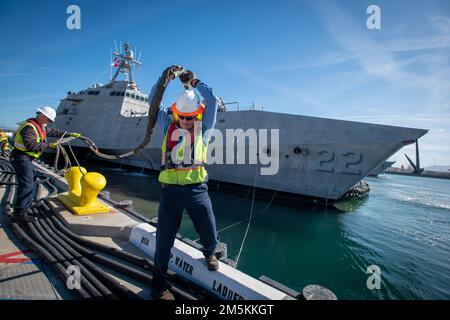 Naval Facilities Engineering Systems Command (NAVFAC) Rigger Dan nach Süden, rechts, manövriert sich vorsichtig unter eine Buglinie, während er und andere NAVFAC-Mitarbeiter daran arbeiten, die USS Kansas City (LCS 22) nach ihrer Ankunft am Naval Surface Warfare Center, Port Hueneme Division, am Dock in Wharf 4 zu sichern. Stockfoto