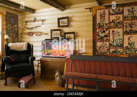 Grüner Ledersessel mit kleinem Ottoman, lange Bank und Aquarium mit Goldfischen im Wohnzimmer mit Wandteppichen im Blockhaus-Stil im Landhausstil. Stockfoto