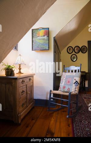 Alte Holzkommode und blau lackierter Schaukelstuhl mit gewebtem Sitz im Korridor oben im rekonstruierten Blockhaus aus den 1840er Jahren. Stockfoto