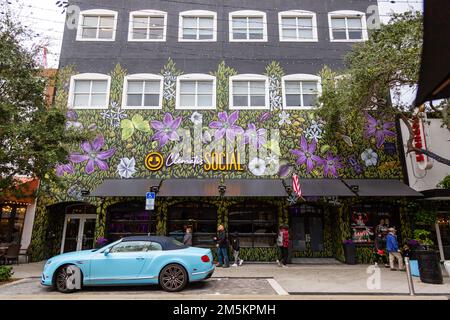 Die Leute passieren ein babyblaues Bentley Continental GT Cabrio, das vor dem Clematis Social Nachtclub im Zentrum von West Palm Beach, Florida, USA, geparkt ist. Stockfoto