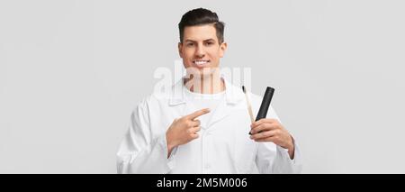 Hübscher junger Mann mit aktivierter Holzkohle-Zahnpasta und Pinsel auf hellem Hintergrund Stockfoto