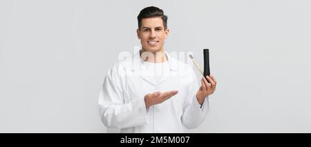 Hübscher junger Mann mit aktivierter Holzkohle-Zahnpasta und Pinsel auf hellem Hintergrund Stockfoto
