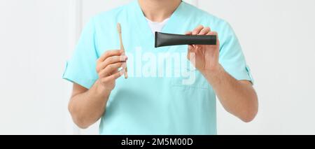 Männlicher Zahnarzt mit Aktivkohle-Zahnpasta und Pinsel auf hellem Hintergrund, Nahaufnahme Stockfoto