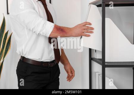 Ein Mann mit Bluterguss, der im Büro einen Ordner auf ein Regal legt Stockfoto