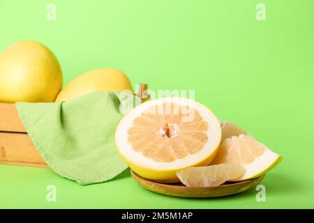 Teller mit Pomelo-Hälften, Scheibe und Korb voller Früchte auf grünem Hintergrund Stockfoto