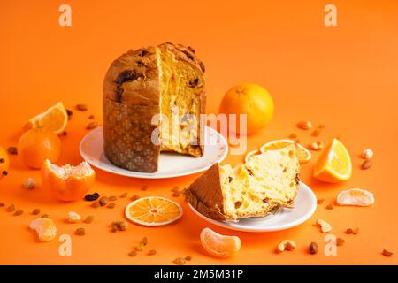 Platten mit geschnittenen Panettone, Zitronen, Nüssen und Rosinen auf orangefarbenem Hintergrund Stockfoto