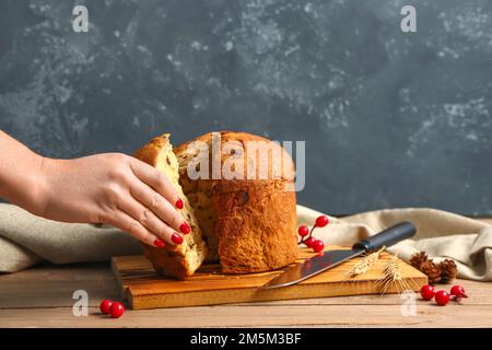 Eine Frau nimmt ein Stück Panettone auf den Tisch, nahe der dunklen Wand Stockfoto