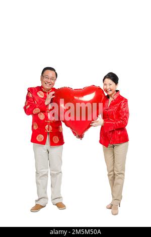 Shed Happy Chinese Silvester Outfit Ältere Paare halten einen roten herzförmigen Ballon Stockfoto