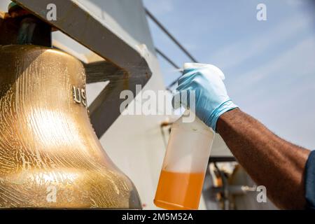 OKINAWA, Japan (24. März 2022) Culinary Specialist 2. Class Tyrie Mordecai aus Savannah, Georgia, sprüht Reinigungslösung auf die Schiffsglocke an Bord des Arleigh Burke-Class Guided Missile Destroyer USS Ralph Johnson (DDG 114). Ralph Johnson ist der Task Force 71/Destroyer Squadron (DESRON) 15, dem größten nach vorn verlegten DESRON der Marine, und der Hauptstreitkraft der US-7.-Flotte zugewiesen. Stockfoto
