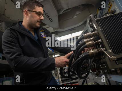 220324-N-XK047-1040 PAZIFIK (24. März 2022) – Aviation Electronics Technician 3. Class Neal Bucholc verbindet ein Kabel mit einem konsolidierten automatisierten Unterstützungssystem (CASS), während ein Funktionstest an Hilfsgeräten auf dem Amphibienschiff USS Makin Island (LHD 8), März 24, durchgeführt wird. Makin Island führt Routineeinsätze in der US-3.-Flotte durch. Stockfoto