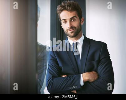 Vertrauen kommt immer vor Erfolg. Verkürztes Porträt eines gutaussehenden jungen Geschäftsmannes, der mit gefalteten Armen im Büro steht. Stockfoto