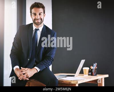 Meine Tür steht immer offen. Abgeschnittenes Porträt eines gutaussehenden jungen Mannes, der auf einem Schreibtisch in seinem Büro sitzt. Stockfoto