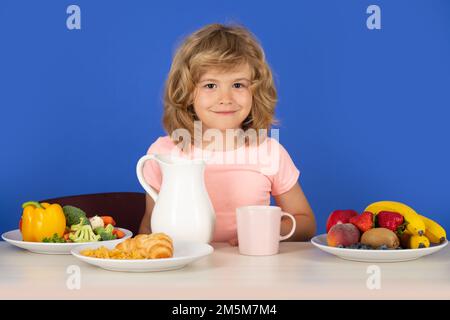 Kind mit Milchmilch. Ein Kind mit Milch wird aus einer Kanne in ein Glas gegossen. Stockfoto