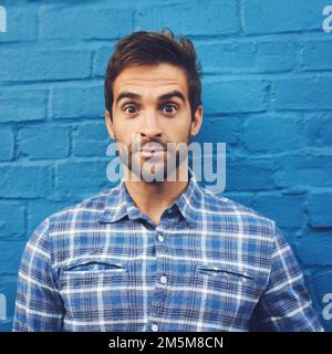 Angenehm überrascht. Ein attraktiver junger Mann, der gegen eine blaue Wand posiert. Stockfoto
