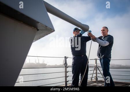 Jakob Kolesik und Naval Surface Warfare Center, Port Hueneme Division Mark (MK) 110 in-Service Engineering Agent Aleksandr Konstantinovsky arbeiten zusammen, um den Lauf der gerade an Bord der USS Kansas City (LCS 2. 22) gereinigten MK 110-Deckpistole auf Hindernisse zu prüfen. Während einer kürzlich stattgefundenen Veranstaltung des Combat Systems Assessment Teams im Kriegsführungszentrum. Stockfoto