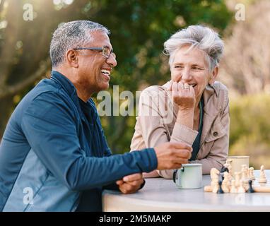 Glücklich, Schach oder ein paar Freunde in der Natur, die ein Brettspiel spielen, sich anfreunden oder über eine lustige Geschichte sprechen. Parken, unterstützen oder gesunde Senioren Stockfoto
