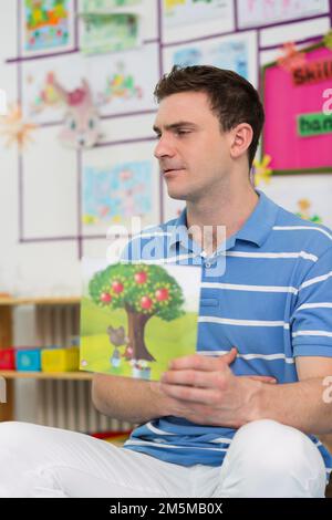 Kindergärtnerinnen, Lehrer und Kinder schauen sich ein Bilderalbum an Stockfoto