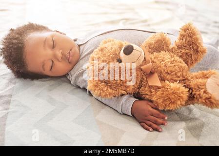 Mit Teddy in der Nähe hat er die sanftesten süßesten Träume. Ein kleiner Junge, der mit einem Teddybär auf einem Bett schläft. Stockfoto