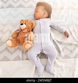 Ruhig schlafen in einem friedlichen Schlaf. Ein kleiner Junge, der mit einem Teddybär auf einem Bett schläft. Stockfoto