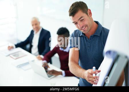 Erfreut darüber, wie gut seine Präsentation läuft. Ein junger Geschäftsmann hält eine Präsentation im Sitzungssaal. Stockfoto