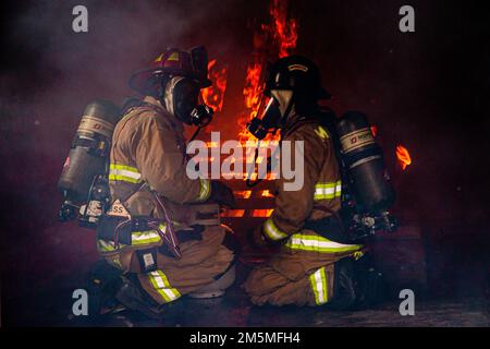 Feuerwehrleute mit Marinekorps-Installationen Pacific Fire and Emergency Services beobachten einen Brand während einer bilateralen Live-Fire-Übung in Camp Hansen, Okinawa, Japan, 25. März 2022. MCIPAC F&ES und die Naha City Fire Department versammelten sich und führten eine Live-Feuerschulung durch, um die verschiedenen Löschtechniken und -Methoden zu vergleichen, die jede Abteilung zur Durchführung derselben Mission einsetzt. Stockfoto