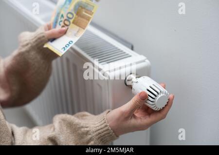 Eine Frau, die Geld vor dem Heizkörper hält. Bezahlung für Heizung im Winter Stockfoto