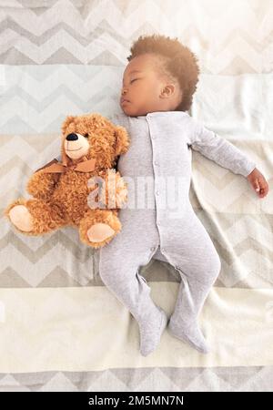 Er ist ins Traumland abgewandert. Ein kleiner Junge, der mit einem Teddybär auf einem Bett schläft. Stockfoto