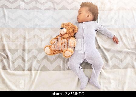 Schlaf ist eine Bärennotwendigkeit des Lebens. Ein kleiner Junge, der mit einem Teddybär auf einem Bett schläft. Stockfoto