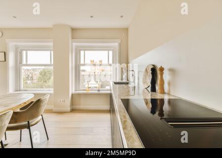 Küche und Essbereich in einem modernen Apartment mit weißen Wänden, Hartholzboden und großen Fenstern mit Blick auf die Stadt Stockfoto