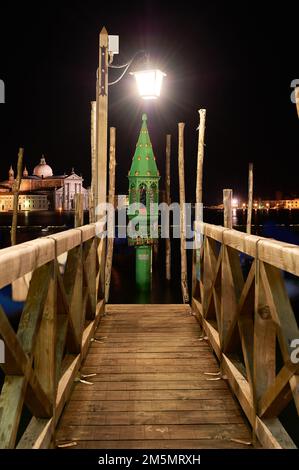 Holzpier zum Andocken venezianischer Gondeln im Dunkeln der Nacht durch Laternen Iluninadas, eine Laterne mit grünem und goldenem Hintergrund Stockfoto