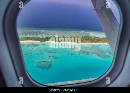 Flugzeugfenster mit wunderschönem Blick auf die Insel Malediven. Luxuriöser Sommerurlaub Tourismus Hintergrund, Blick aus dem Flugzeugfenster. Atollinseln Stockfoto