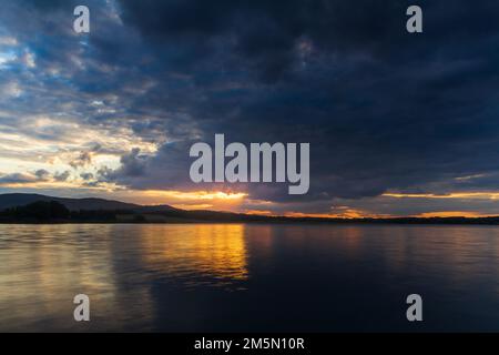 Majestätischer Sonnenuntergang, dramatischer Himmel über dem Teich und dem fernen hil. Tschechische Landschaft, lange Exposition Stockfoto