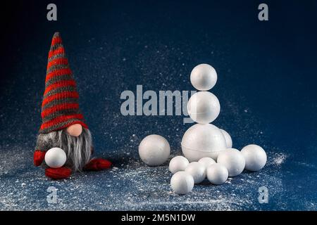 Weihnachtsdekoration Elf, Zwerg mit Schneeball und Schneemann bauen. Winterfestival-Konzept, Hintergrundszene für Feiertage Stockfoto