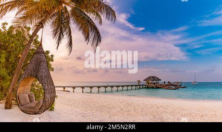 Romantisches tropisches Sonnenuntergang-Strandpanorama als Sommerlandschaft mit entspannender Strandschaukel oder Hängematte auf Kokospalmen, weißem Sand und ruhigem Strandbanner Stockfoto