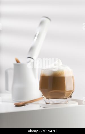 Cappuccino in einem Glasbecher auf einem weißen Holztisch, Kaffee und Milchschaum. Stockfoto