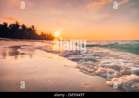 Fantastischer Blick aus der Nähe auf die ruhigen Meerwasserwellen mit orangefarbenem Sonnenaufgang Sonnenuntergang. Tropische Inselstrandlandschaft, exotische Küste. Sommerurlaub Stockfoto