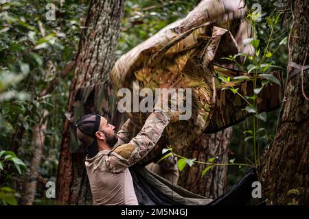 USA Air Force Tech. Sergeant Michael Galindo, 38. Rettungsschwadron Blue Team, Pararescueman, baut einen Regenfall über seiner Hängematte im Dschungel von Wahiawa, Hawaii, auf, 28. März 2022. Galindo und seine Teamkollegen mussten Hängematten aufstellen, um sich von Tausendfüßlern, Spinnen und anderen gefährlichen Tieren fernzuhalten, während sie schliefen. Die 38. RQS Blue Team Pararescuemen trainierten in der Dschungelkriegsführung, um die Rettungstaktiken, -Techniken und -Verfahren des Personals für die Region Indo-Pazifik anzupassen. Stockfoto