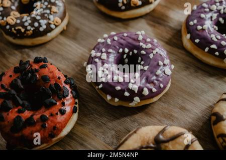 Eine Nahaufnahme frisch gebackener Donuts, glasiert mit Schokolade und Vanille, anders dekoriert, serviert auf einem Holzbrett Stockfoto